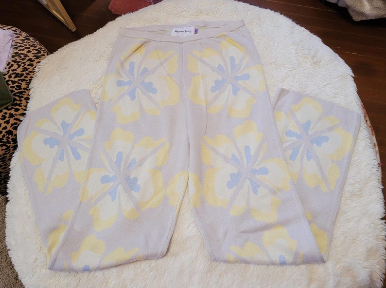 Puede incluir: Pantalones de punto lila claro con un estampado floral en amarillo y azul claro. Los pantalones tienen un dise&ntilde;o de pierna ancha y un ajuste c&oacute;modo y relajado. El estampado floral est&aacute; distribuido uniformemente por los pantalones. La etiqueta dice 'House of Sunny'.