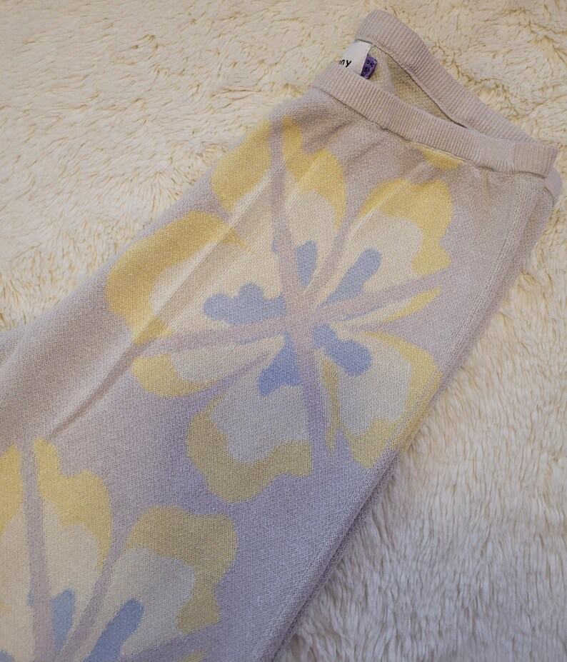 Puede incluir: Pantalones de punto lila claro con un estampado floral en amarillo y azul claro. Los pantalones tienen una cintura acanalada y un aspecto suave y texturizado. El dise&ntilde;o floral es un patr&oacute;n repetido en la tela.