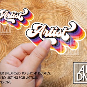 May include: Two die-cut stickers featuring the word Artist in a white cursive font with a thick black outline. Behind the text are layered, repeating drop shadows in shades of purple, blue, green, yellow, orange, and red, creating a vibrant effect.