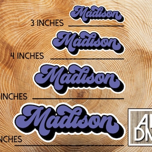 May include: A selection of retro-style stickers featuring the name "Madison" in purple and black. Sizes available are 7.6, 10.2, 12.7, and 15.2 cm. The background is a wood grain pattern. The logo "AEDM" is in the bottom right corner.