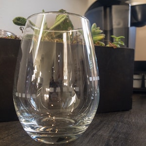 May include: A clear glass with a rounded bottom and a wide mouth. The glass has a pattern of small squares etched into the side.
