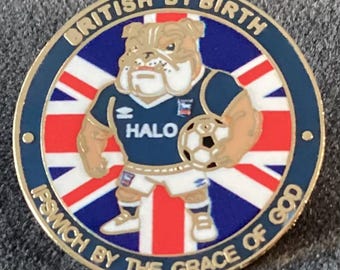May include: A circular metal pin featuring a bulldog wearing a blue football jersey with the text HALO, holding a football. The background is a Union Jack flag. The border text reads BRITISH BY BIRTH and IPSWICH BY THE GRACE OF GOD in gold.