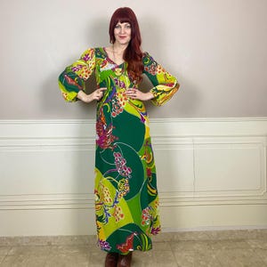 Peut inclure: Une longue robe fluide avec un motif floral vibrant et coloré. La robe présente un décolleté en V et de longues manches cloche. Les couleurs dominantes sont le vert, le jaune et le rose, créant un design audacieux. La robe est de style vintage.