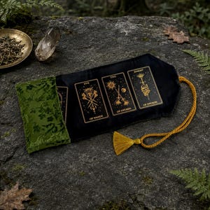 Może przedstawiać: Czarny aksamitny woreczek na karty tarota ze złotymi ilustracjami kart Five of Wands, Two of Swords oraz Knight of Swords. Woreczek posiada klapkę z zielonego aksamitu oraz złoty pleciony sznurek z pasującym chwostem.
