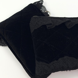 May include: Two black velvet pouches with quilted stitching. The pouches are trimmed with delicate black lace along the top edges. One pouch has a silver ring attached. The pouches are on a white background.