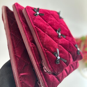 以下が含まれることがあります： 黒のリボンとラインストーンが付いた、3つの濃い赤色のベルベット製のジッパー付きポーチ。ポーチはキルティングされており、柔らかく高級感のある肌触りです。