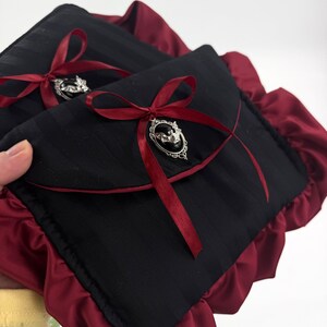 May include: Two black, striped fabric pouches with burgundy satin trim and bows. Each pouch has a silver-toned brooch with a bat design. The bows are made of burgundy ribbon.
