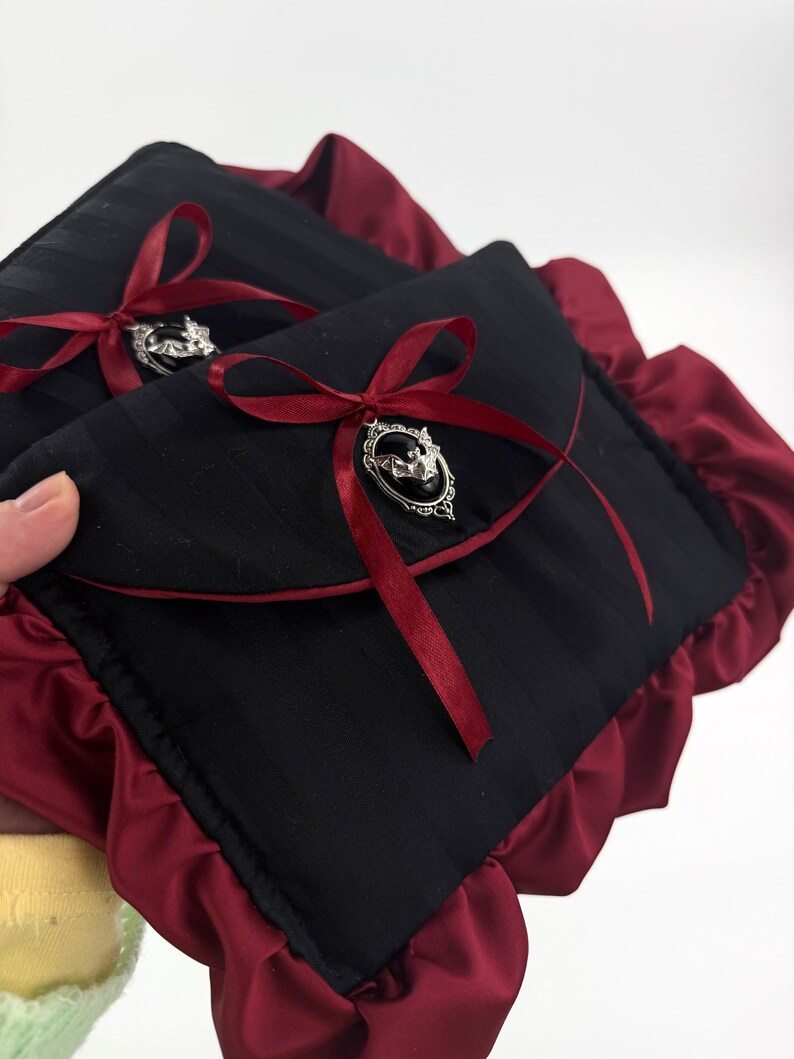 May include: Two black, striped fabric pouches with burgundy satin trim and bows. Each pouch has a silver-toned brooch with a bat design. The bows are made of burgundy ribbon.