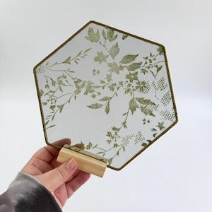 May include: A hexagonal mesh display panel featuring a green botanical leaf and floral pattern. The mesh is framed in a thin green border and is supported by a small, rectangular light-colored wooden base stand for upright positioning.