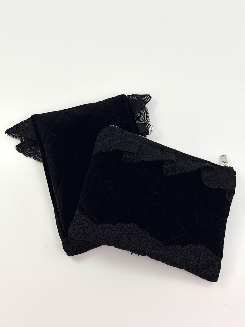 May include: Two black velvet zippered pouches with quilted stitching and decorative lace trim. The pouches are in a folded arrangement, showcasing the texture and design. The zippers are silver-toned.