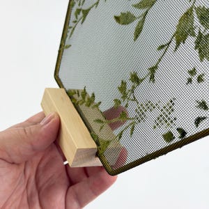 May include: A rectangular display panel featuring a fine black mesh screen with a printed green botanical leaf pattern. The mesh is framed in a thin dark border and is securely slotted into a light-colored, unfinished wooden base stand.