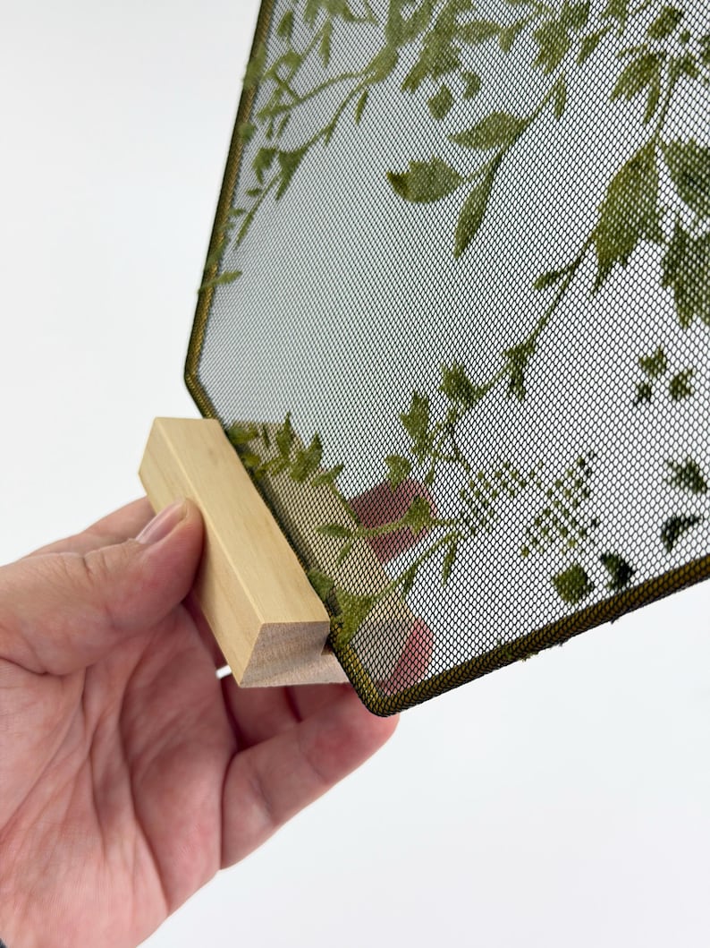 May include: A rectangular display panel featuring a fine black mesh screen with a printed green botanical leaf pattern. The mesh is framed in a thin dark border and is securely slotted into a light-colored, unfinished wooden base stand.