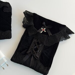 May include: Black velvet pouch with lace trim and a ribbon tie closure. The pouch features a decorative cross with a red gem and a black bow. The design is gothic-inspired.