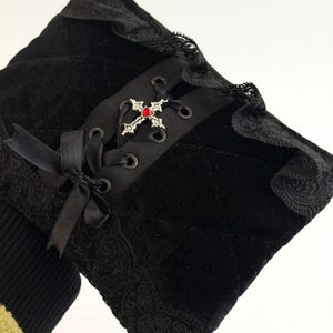 May include: Black velvet sleeve with lace trim and a decorative cross. The sleeve features a quilted pattern, a black ribbon bow, and a silver cross with a red gem. The design has a gothic aesthetic.