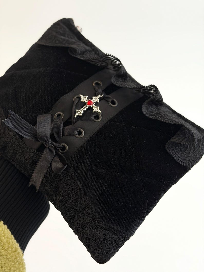 May include: Black velvet sleeve with lace trim and a decorative cross. The sleeve features a quilted pattern, a black ribbon bow, and a silver cross with a red gem. The design has a gothic aesthetic.