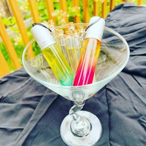 Pode incluir: Três garrafas de vidro com rolo, tampas prateadas e líquidos coloridos dentro. As garrafas estão em uma taça de martini de vidro transparente.