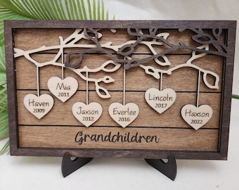 May include: A wooden plaque with a carved tree branch design and hanging hearts. Each heart has a name and year engraved on it. The names are Haven 2009, Mia 2011, Jaxson 2012, Everlee 2016, Lincoln 2017, and Haxson 2022. The plaque reads "Grandchildren" at the bottom.