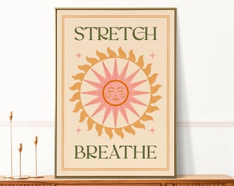 May include: A framed art print with a beige background and a sun design in pink and orange. The words "STRETCH" and "BREATHE" are in green. The art has a retro, bohemian style.
