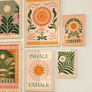 May include: Set of six framed prints with a whimsical, retro aesthetic. Each print features a sun with a face, surrounded by stylised flowers, leaves, and stars. The prints have a peach background with gold frames. The text on the prints includes "Breathe Deeper", "Inhale Exhale", "Dreamer", "Lunefleur", "Fleurs au Soleil", and "Breathe Deeper".