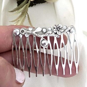 May include: A silver-toned hair comb with a floral and leaf design. The comb features clear, sparkling rhinestones and a small flower. The comb's teeth are evenly spaced and the overall design is delicate and elegant.