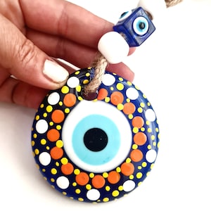 May include: A blue and white evil eye charm with orange and yellow polka dots. The charm is attached to a string with white and blue beads.