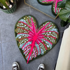 May include: A heart-shaped rug with a pink and green leaf design. The rug is made of a soft, plush material and has a textured surface.