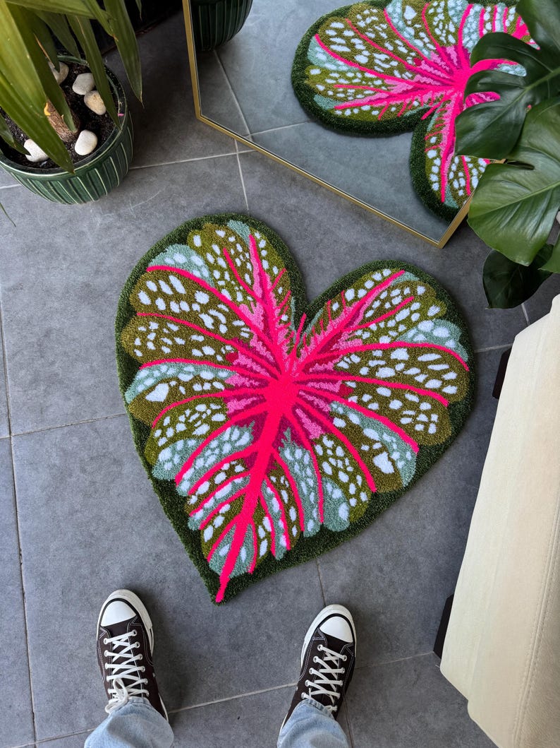 May include: A heart-shaped rug with a pink and green leaf design. The rug is made of a soft, plush material and has a textured surface.