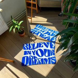 Peut inclure: Tapis de bain bleu et blanc avec le texte "Believe in your dreams" dans une police de caract&egrave;res stylis&eacute;e.