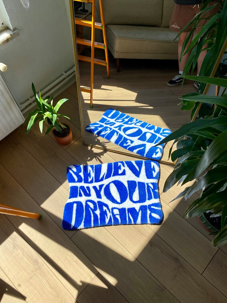 Peut inclure: Tapis de bain bleu et blanc avec le texte "Believe in your dreams" dans une police de caract&egrave;res stylis&eacute;e.