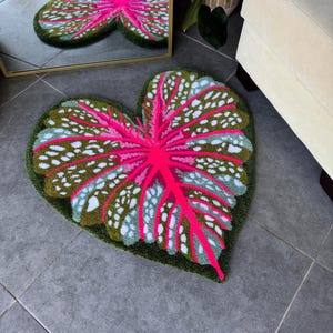 May include: A heart-shaped rug with a pink and green leaf design. The rug is made of a soft, plush material and has a raised texture.