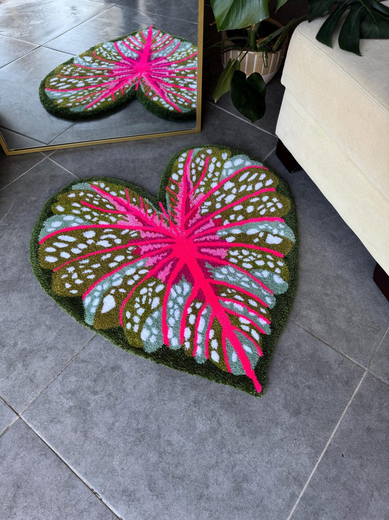 May include: A heart-shaped rug with a pink and green leaf design. The rug is made of a soft, plush material and has a raised texture.
