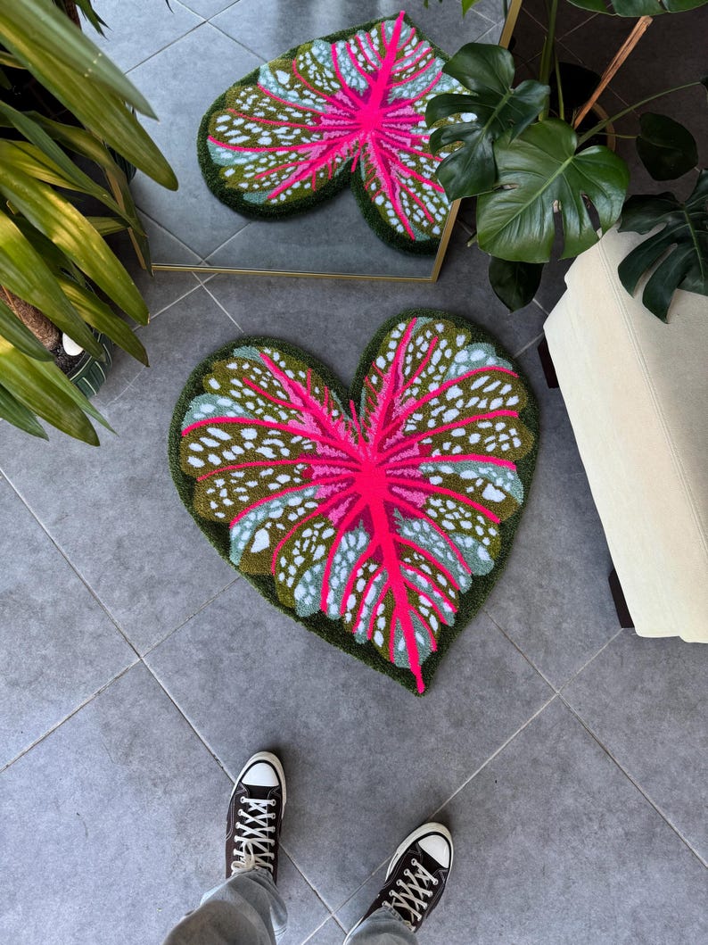 May include: A pink and green heart-shaped rug with a leaf design. The rug is made of a soft, plush material and has a white border.