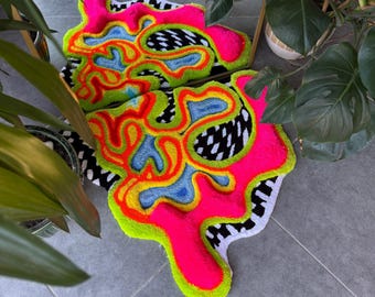 Puede incluir: Una alfombra abstracta colorida con un diseño rosa, verde, amarillo y azul. La alfombra tiene un borde a cuadros blanco y negro.