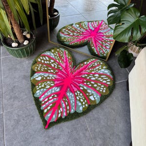 May include: A green and pink leaf-shaped rug with white spots. The rug is made of a soft, plush material and has a realistic leaf design.
