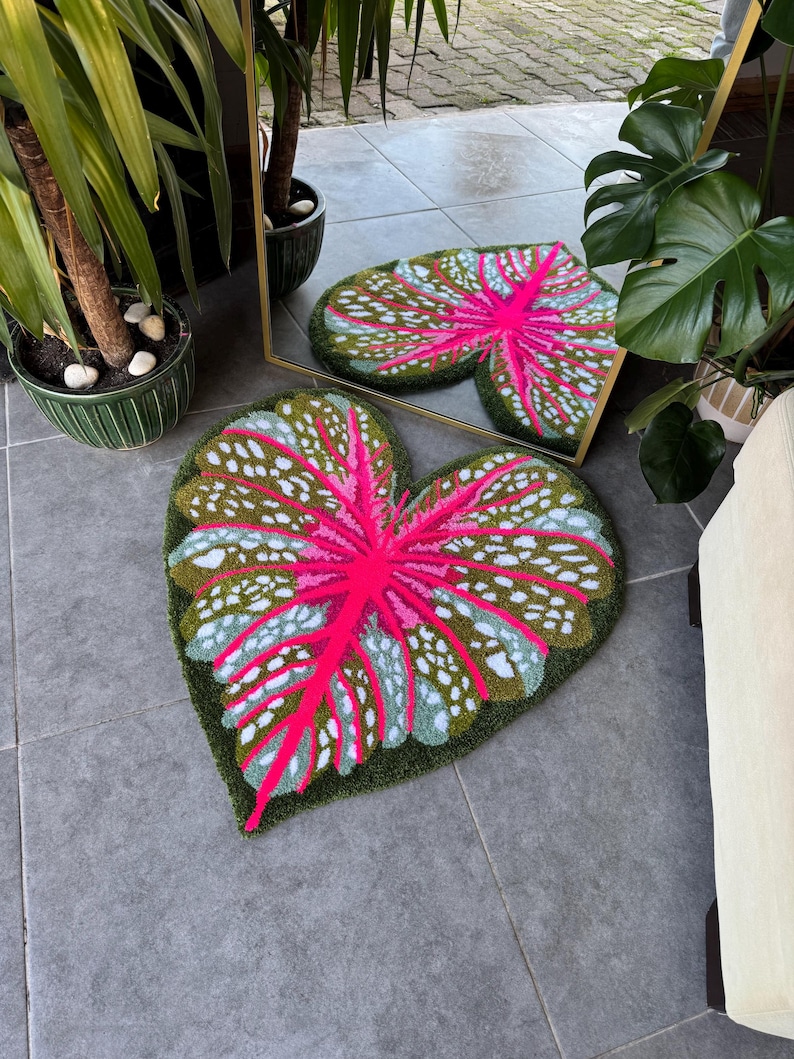 May include: A green and pink leaf-shaped rug with white spots. The rug is made of a soft, plush material and has a realistic leaf design.