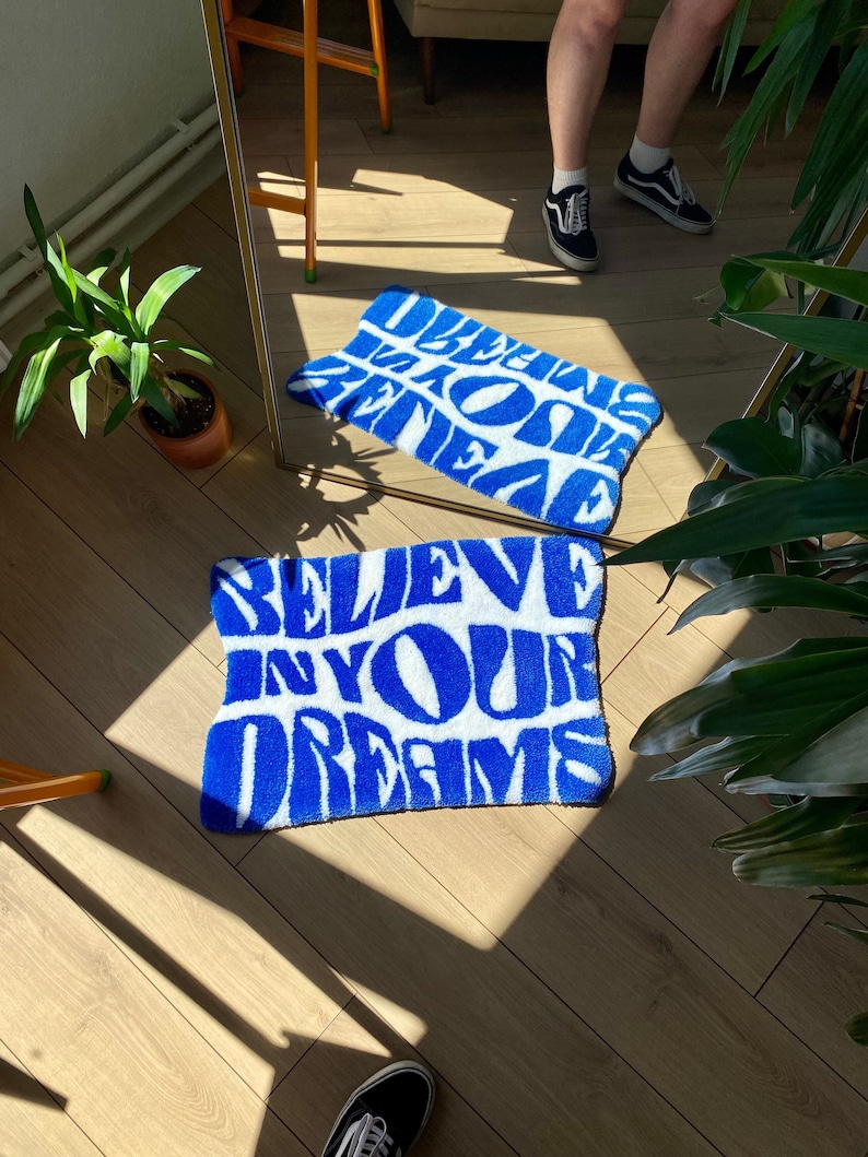 Peut inclure: Un tapis de bain bleu et blanc avec le texte "Believe in your dreams" dans une police de caract&egrave;res audacieuse et stylis&eacute;e.