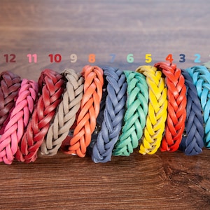 May include: Twelve braided leather bracelets in various colours, including red, pink, beige, orange, blue, green, and yellow. The bracelets are numbered 1 through 12.