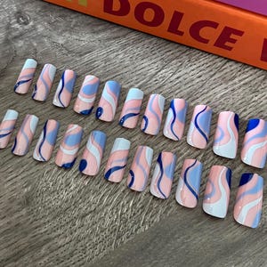 May include: Set of 14 false nails with a pink, blue and white abstract swirl design. The nails are rectangular and have a glossy finish.