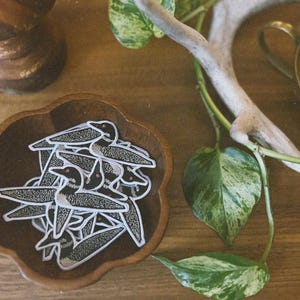 Puede incluir: Un cuenco de madera lleno de parches de p&aacute;jaros loon negros y blancos. Los parches est&aacute;n dispuestos en una pila, con algunos de los p&aacute;jaros mirando hacia arriba y otros hacia abajo.