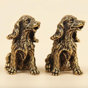 Peut inclure: Deux figurines de chien identiques en m&eacute;tal avec une finition bronze fonc&eacute;. Chaque statue repr&eacute;sente un chien de type &eacute;pagneul assis avec de longues oreilles textur&eacute;es, la gueule entrouverte et un pelage d&eacute;taill&eacute;. Les figurines sont c&ocirc;te &agrave; c&ocirc;te.