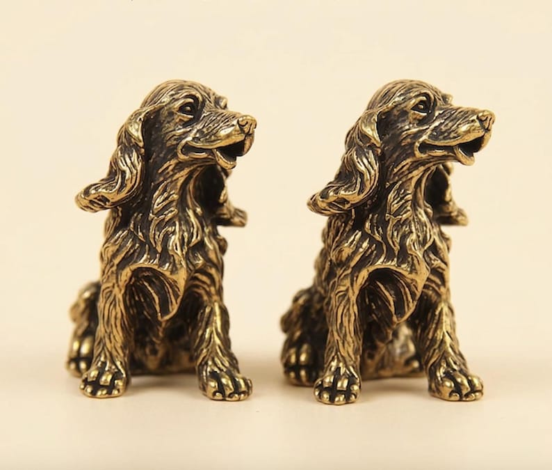 Peut inclure: Deux figurines de chien identiques en m&eacute;tal avec une finition bronze fonc&eacute;. Chaque statue repr&eacute;sente un chien de type &eacute;pagneul assis avec de longues oreilles textur&eacute;es, la gueule entrouverte et un pelage d&eacute;taill&eacute;. Les figurines sont c&ocirc;te &agrave; c&ocirc;te.
