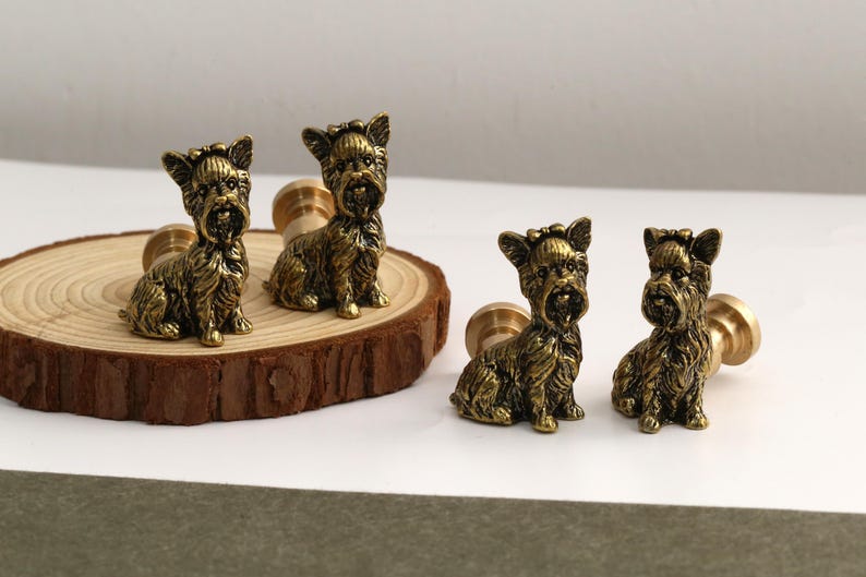 Peut inclure: Quatre boutons de placard en laiton antique en forme de chiens Yorkshire Terrier assis. Chaque bouton pr&eacute;sente un pelage textur&eacute; d&eacute;taill&eacute; et un petit n&oelig;ud sur la t&ecirc;te, avec une tige de fixation cylindrique &agrave; l'arri&egrave;re de chaque figurine.