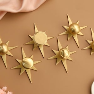 May include: A set of five gold-coloured metal cabinet knobs, each featuring a central circular knob mounted on a starburst-shaped backplate with multiple pointed rays extending outward in a symmetrical, geometric design with a smooth finish.