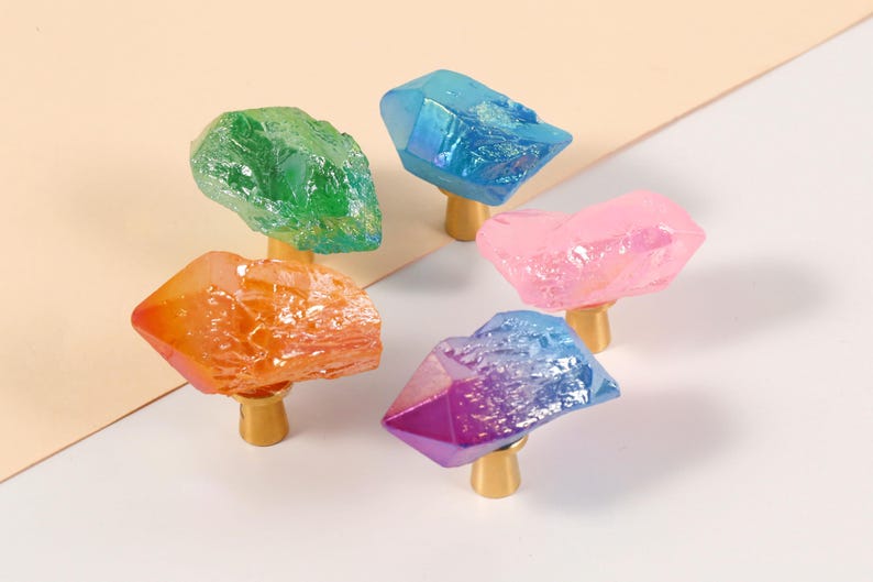 Peut inclure: Cinq boutons de meuble en cristal color&eacute; dans les tons de vert, orange, bleu, rose et violet. Chaque bouton a une base dor&eacute;e. Les cristaux ont un aspect rugueux et textur&eacute;.