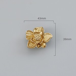 May include: Gold-toned metal flower-shaped drawer pull with a detailed design. The pull measures 43mm wide and 39mm high.