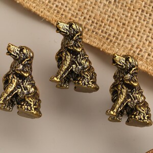 Peut inclure: Trois petites figurines en m&eacute;tal de couleur laiton antique repr&eacute;sentant des chiens assis. Chaque figurine pr&eacute;sente une texture de fourrure d&eacute;taill&eacute;e et une posture avec la t&ecirc;te lev&eacute;e, finie avec une patine sombre et vieillie qui souligne les traits sculpt&eacute;s.