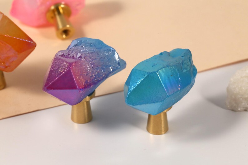 Peut inclure: Gros plan sur des boutons de meubles d&eacute;coratifs avec des formations cristallines. Les boutons pr&eacute;sentent une vari&eacute;t&eacute; de couleurs, dont le bleu, le violet et le rose, avec des bases dor&eacute;es. Ces boutons uniques ajoutent une touche d'&eacute;l&eacute;gance.