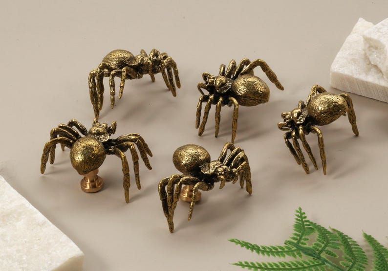 May include: Five antique brass spider cabinet knobs. Each knob features a detailed spider design with eight legs and a textured body. The knobs are mounted on a brass base and are suitable for furniture or decorative use.