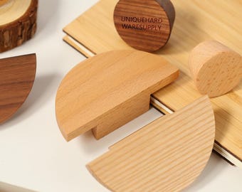 May include: Several semi-circular and cylindrical wooden furniture handles in light and dark wood tones. One dark circular handle features the text UNIQUEHARD WARESUPPLY. The pieces are arranged on a light-colored surface with visible wood grain.