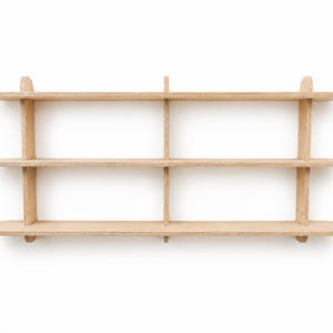 May include: A wall-mounted light-colored wooden shelving unit featuring three horizontal shelves with rounded ends. The structure is supported by three vertical dividers that intersect the shelves, creating six distinct storage compartments.
